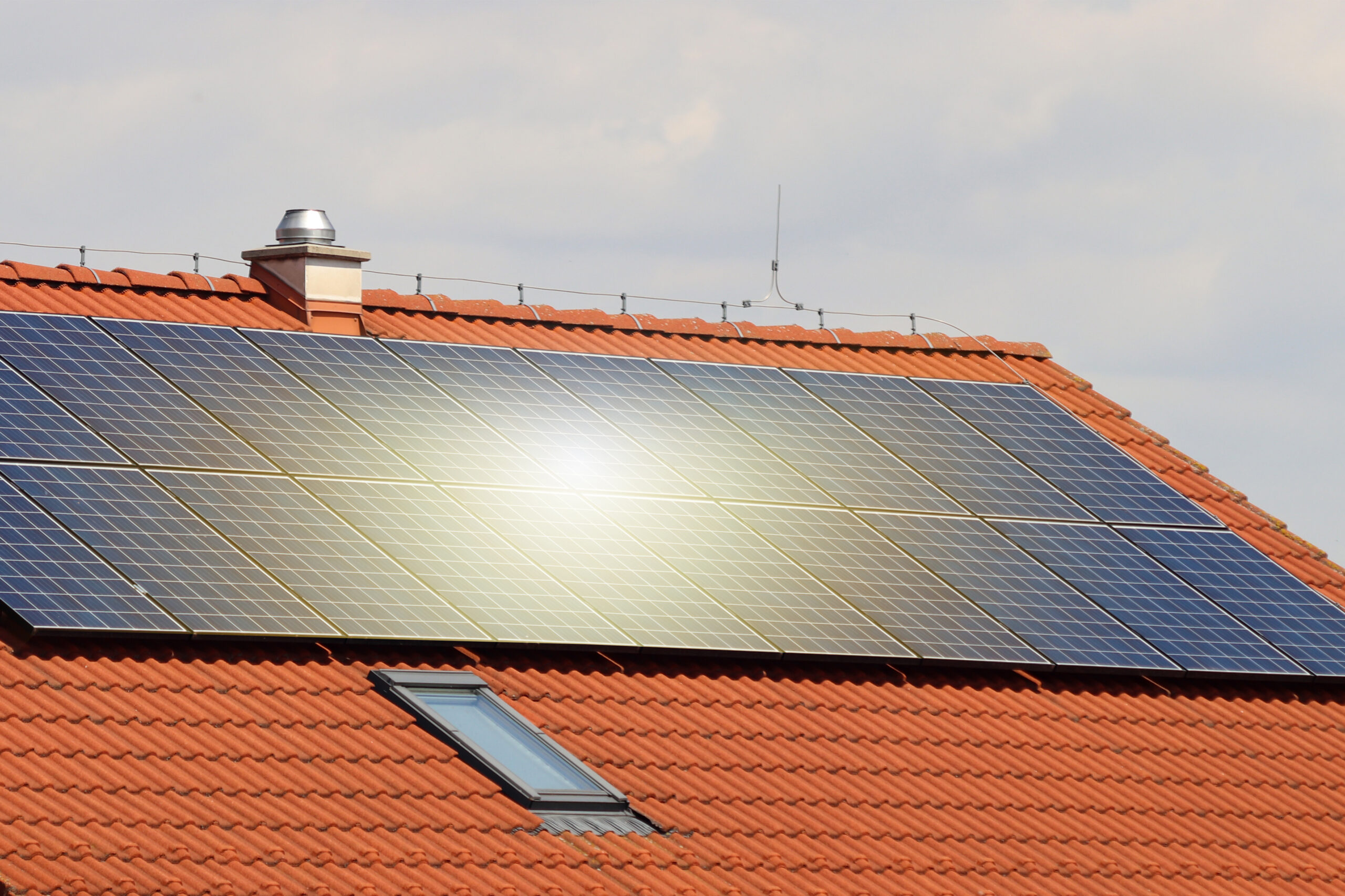 Photovoltaic or solar panels on roof of the house at sunset. Red roof with ecological solar system during the summer day. Clouds in the background.